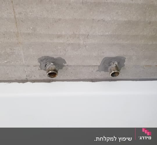 שני צינורות מתכת מותקנים בקיר בטון